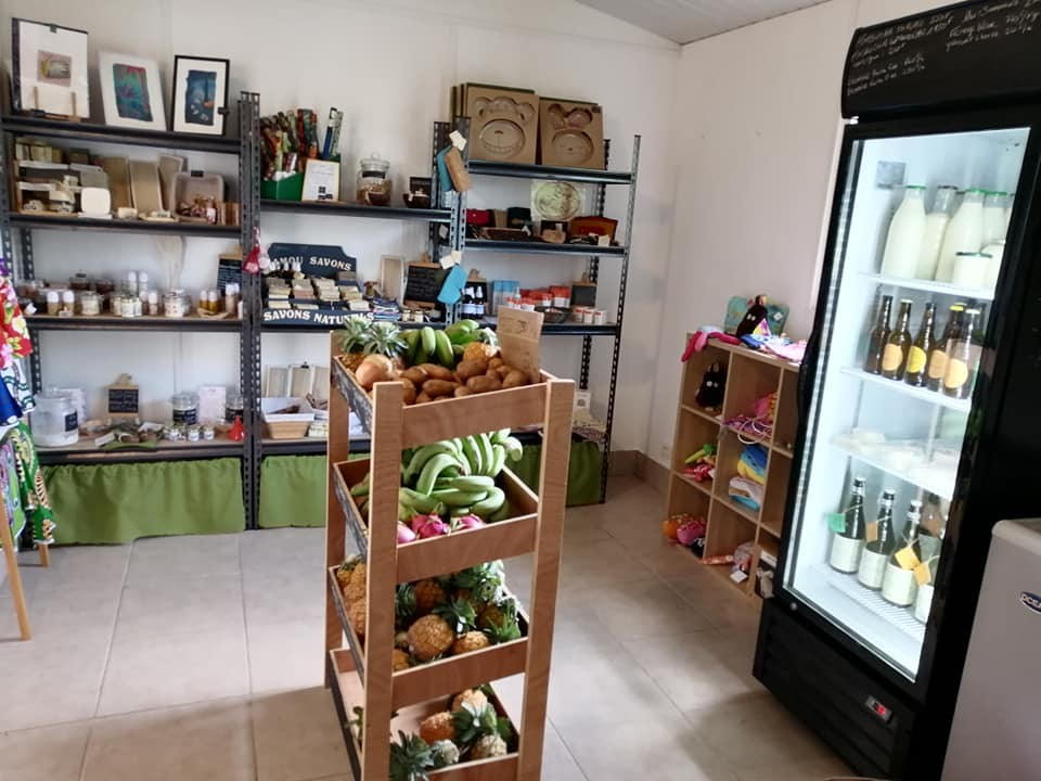 Intérieur de la boutique : étagères de produits, présentoir de fruits et réfrigérateur.